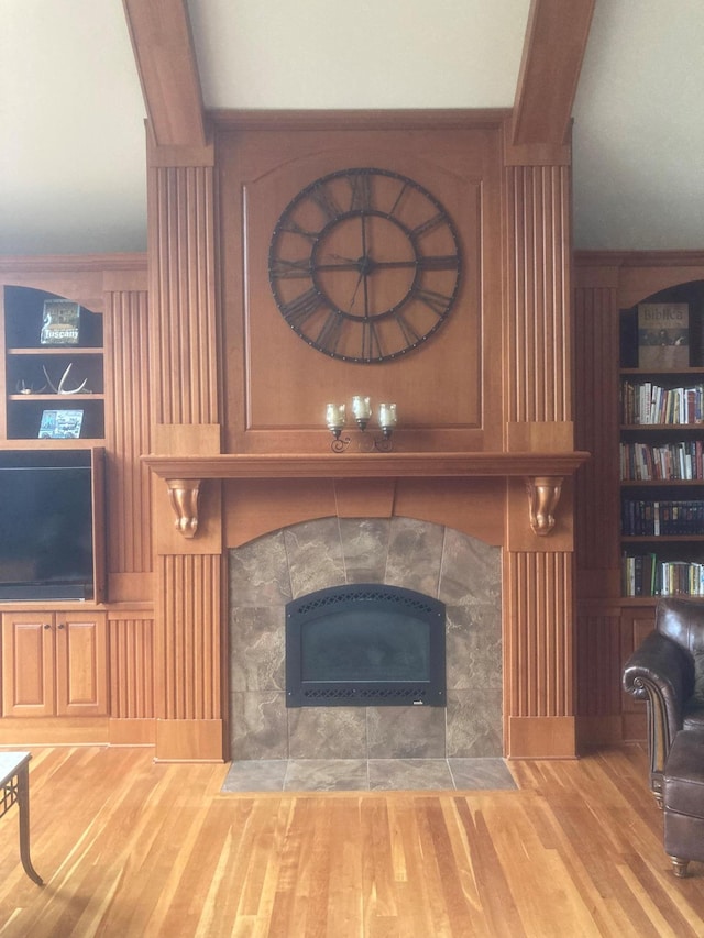 living room featuring beamed ceiling, a tiled fireplace, and wood finished floors