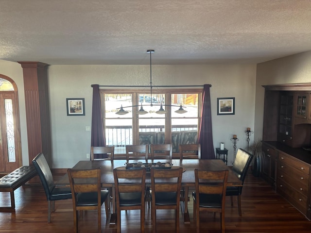 dining room featuring a textured ceiling, dark wood-type flooring, and decorative columns