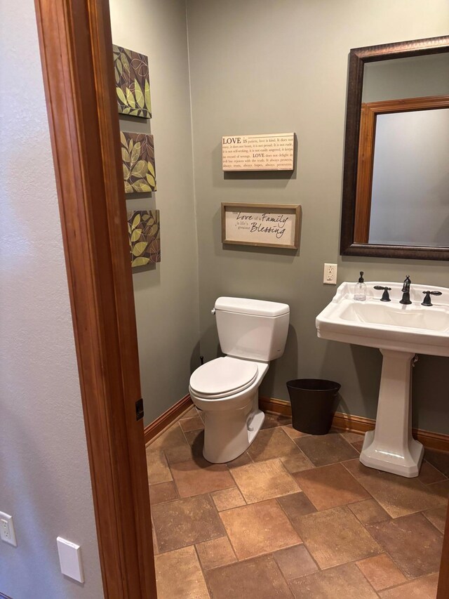 bathroom with toilet, stone tile flooring, and baseboards