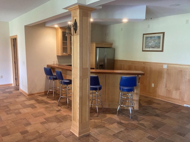 bar featuring a dry bar, a wainscoted wall, stainless steel refrigerator with ice dispenser, and wood walls