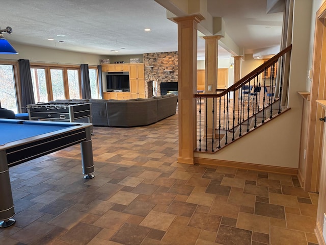 game room featuring a fireplace, decorative columns, stone finish floor, a textured ceiling, and baseboards