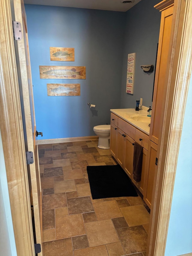 bathroom featuring toilet, stone finish flooring, baseboards, and vanity