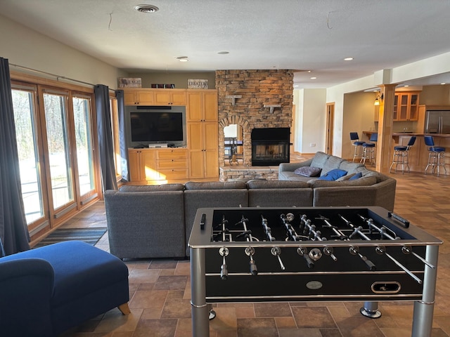 living room featuring a textured ceiling, a stone fireplace, stone finish floor, and visible vents