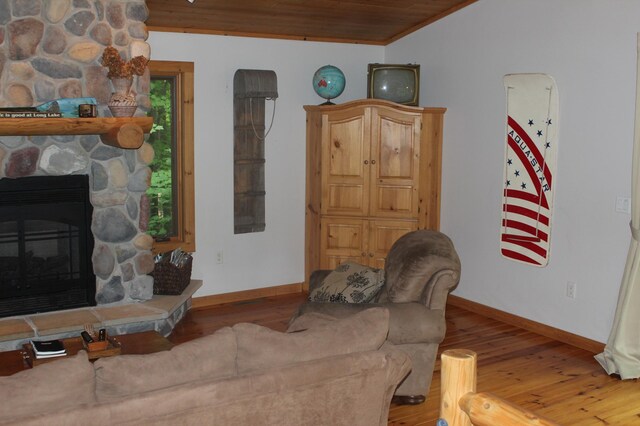 living room featuring a stone fireplace, wooden ceiling, wood finished floors, and baseboards