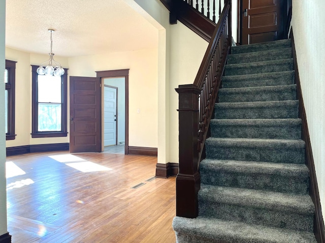 staircase with an inviting chandelier, a textured ceiling, baseboards, and wood finished floors