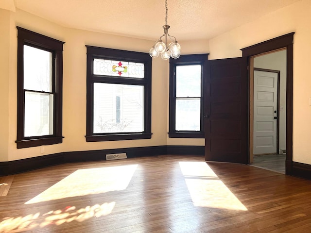 unfurnished room featuring a textured ceiling, visible vents, a chandelier, and wood finished floors