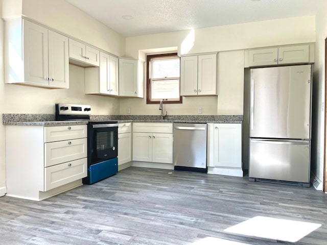 kitchen with appliances with stainless steel finishes, white cabinetry, light wood-style flooring, and a textured ceiling