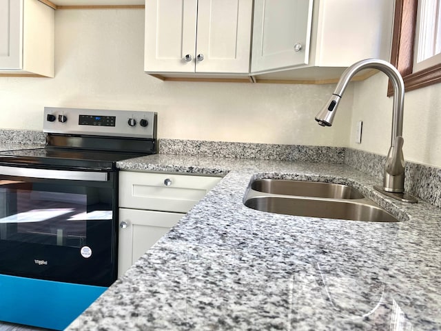 kitchen with light stone counters, white cabinets, range with electric stovetop, and a sink