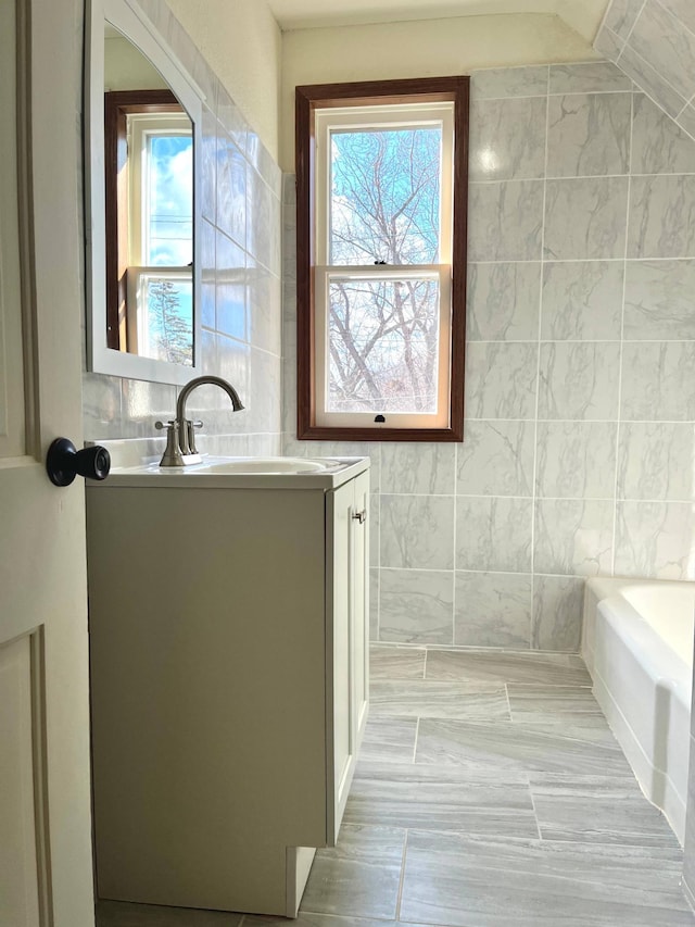 full bathroom with a washtub, tile walls, and vanity