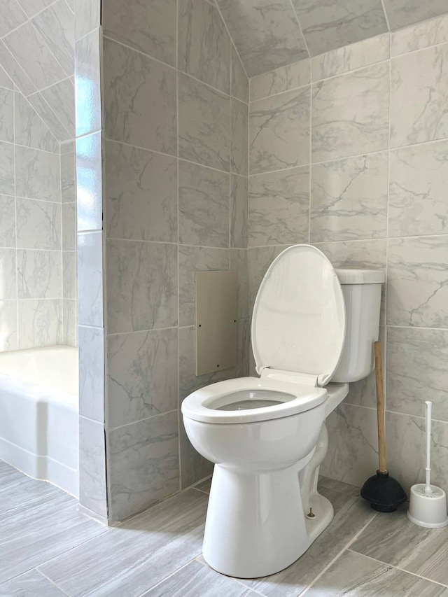 bathroom featuring toilet, tile walls, and a bath