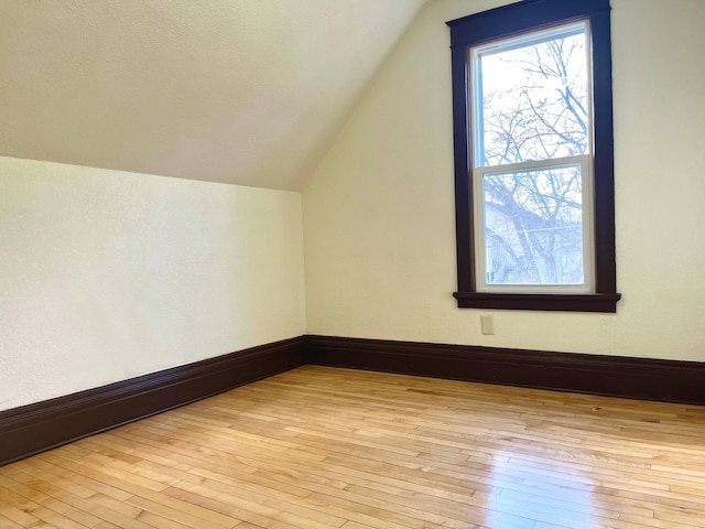 additional living space featuring vaulted ceiling, light wood-type flooring, and baseboards