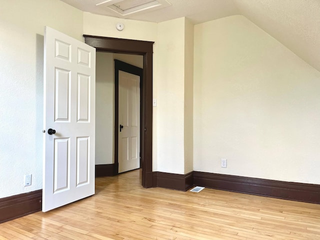 additional living space with attic access, visible vents, baseboards, lofted ceiling, and light wood-style floors