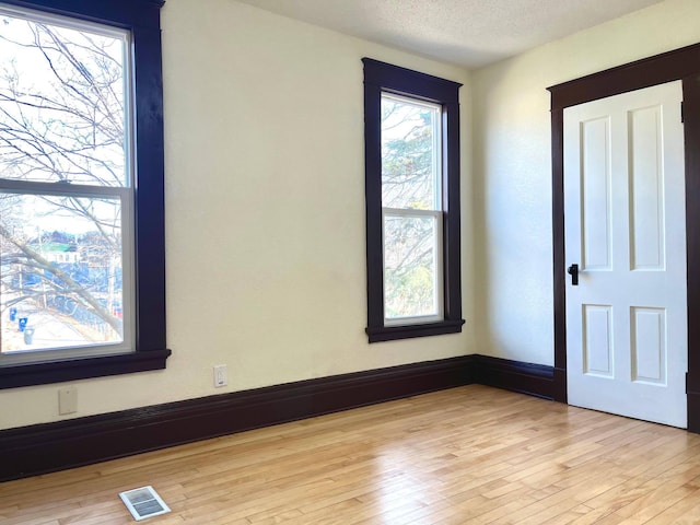 empty room featuring baseboards, visible vents, light wood-style flooring, and a textured ceiling