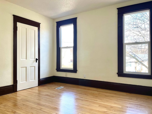 spare room featuring visible vents, baseboards, a textured ceiling, and light wood finished floors