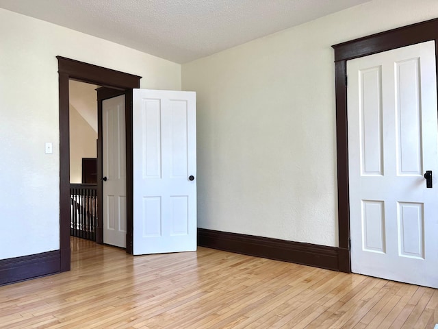 unfurnished bedroom featuring a textured ceiling, light wood-style flooring, and baseboards