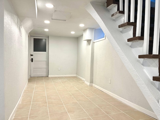 basement featuring baseboards, a textured wall, stairway, tile patterned flooring, and recessed lighting