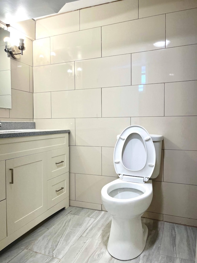 half bath with toilet, tile walls, and vanity