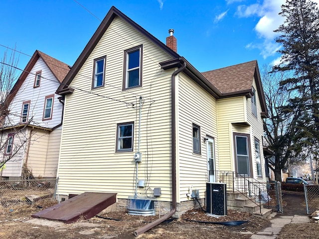 back of house with a chimney, fence, and roof with shingles