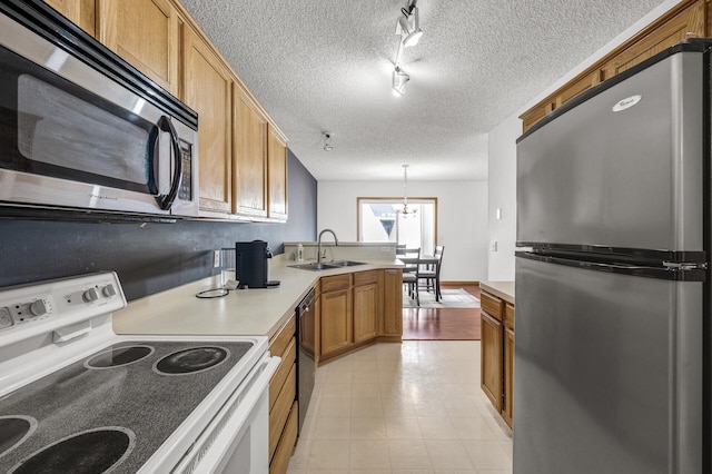 kitchen featuring a sink, a textured ceiling, appliances with stainless steel finishes, a peninsula, and light countertops