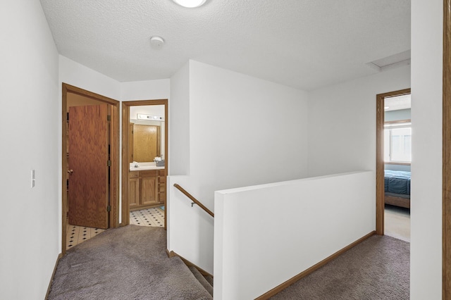 corridor with baseboards, carpet floors, attic access, a textured ceiling, and an upstairs landing