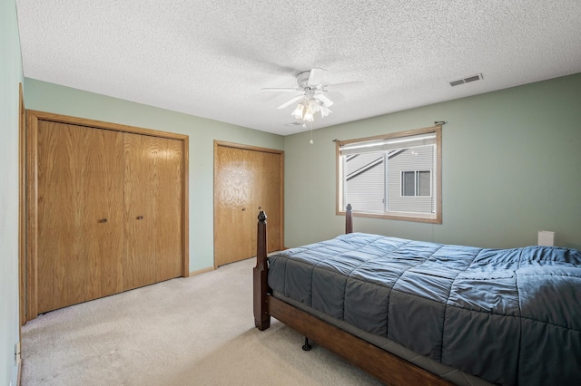 bedroom with visible vents, multiple closets, a ceiling fan, a textured ceiling, and light colored carpet