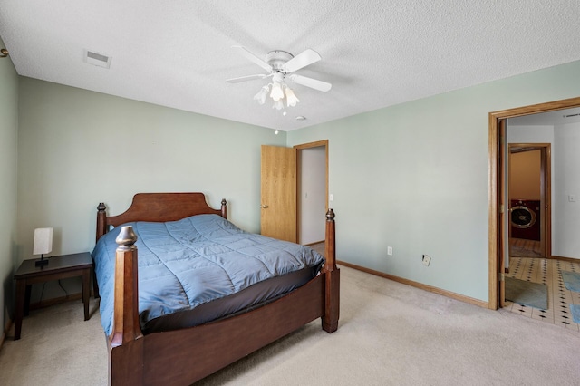 bedroom featuring visible vents, washer / clothes dryer, a textured ceiling, baseboards, and light colored carpet