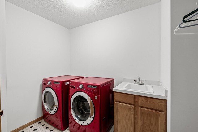 laundry room with a sink, a textured ceiling, washing machine and dryer, cabinet space, and light floors