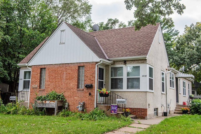 bungalow with entry steps, roof with shingles, a front lawn, and brick siding