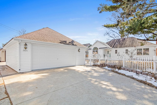 view of property exterior with a fenced front yard, a garage, an outbuilding, and roof with shingles