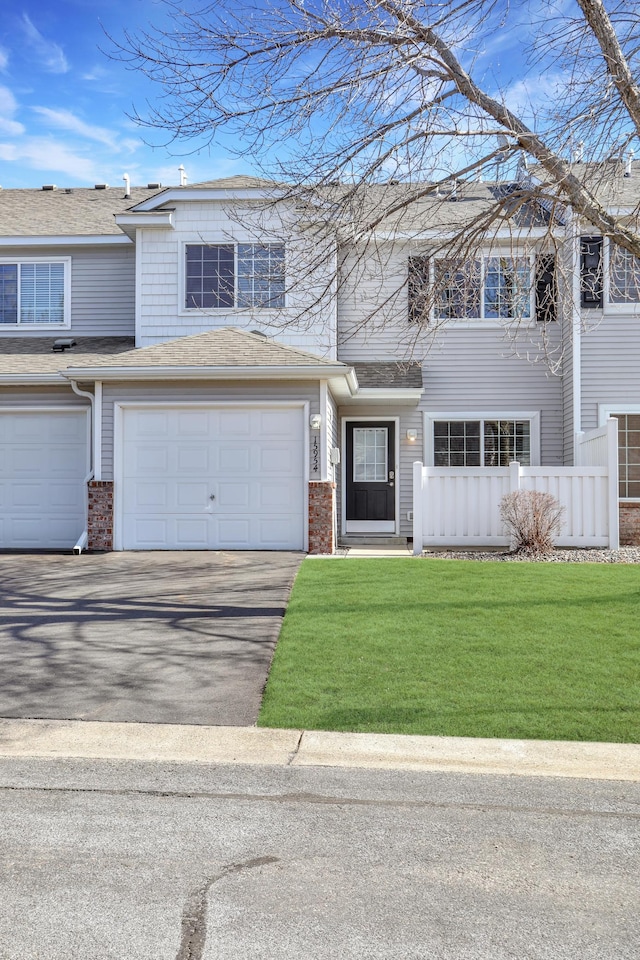 view of property with aphalt driveway, brick siding, fence, and a front lawn