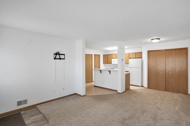 unfurnished living room featuring a textured ceiling, light carpet, visible vents, and baseboards