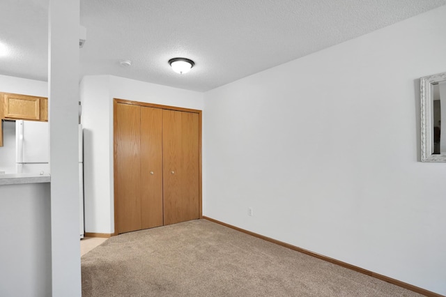 unfurnished bedroom featuring a textured ceiling, carpet flooring, baseboards, a closet, and freestanding refrigerator