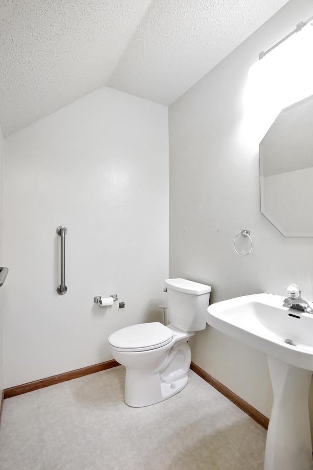bathroom with lofted ceiling, a textured ceiling, toilet, and baseboards