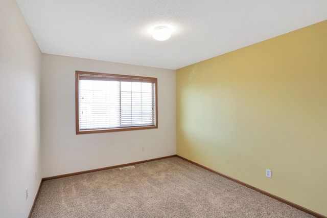 carpeted spare room with visible vents, baseboards, and a textured ceiling
