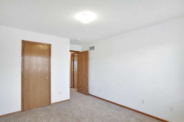 unfurnished bedroom with visible vents, baseboards, light colored carpet, a textured ceiling, and a closet
