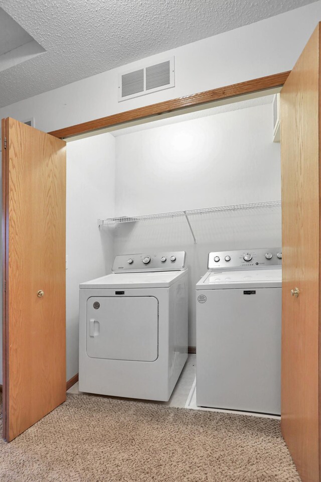 clothes washing area with laundry area, visible vents, washer and clothes dryer, and a textured ceiling