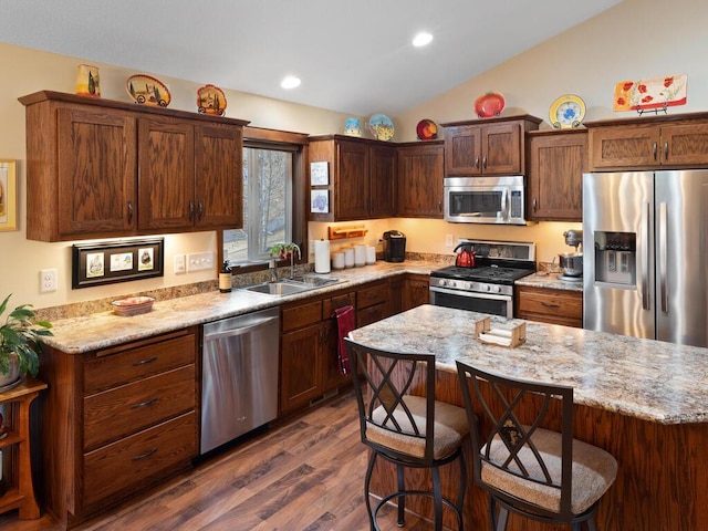 kitchen with dark wood finished floors, lofted ceiling, appliances with stainless steel finishes, a breakfast bar, and a sink