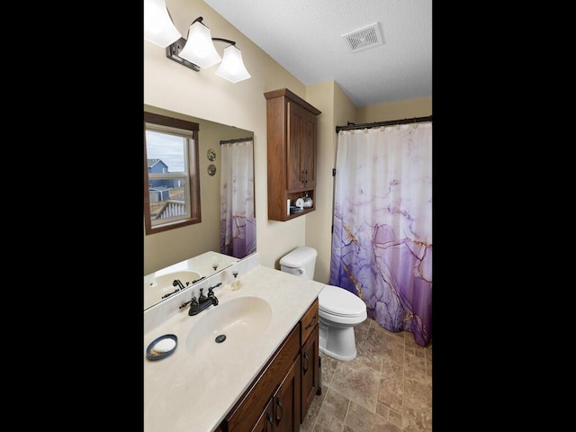 bathroom with visible vents, toilet, stone finish flooring, vanity, and a textured ceiling