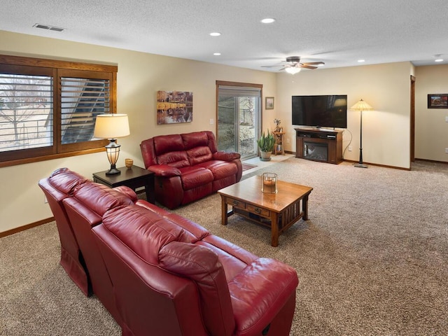 living room featuring a textured ceiling, carpet, a glass covered fireplace, and visible vents