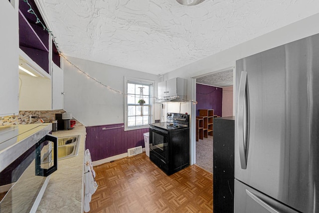 kitchen featuring wainscoting, black electric range oven, freestanding refrigerator, light countertops, and a textured ceiling