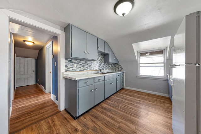 kitchen featuring gray cabinetry, light countertops, freestanding refrigerator, decorative backsplash, and dark wood-style floors