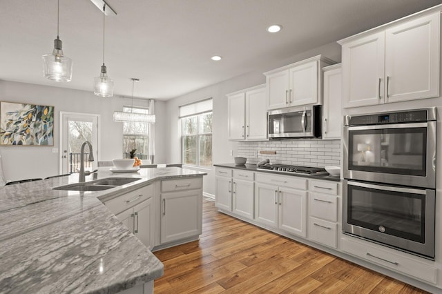 kitchen featuring light wood finished floors, tasteful backsplash, stainless steel appliances, white cabinetry, and a sink