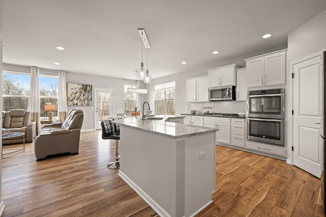 kitchen featuring open floor plan, decorative backsplash, light wood-style flooring, stainless steel appliances, and a sink