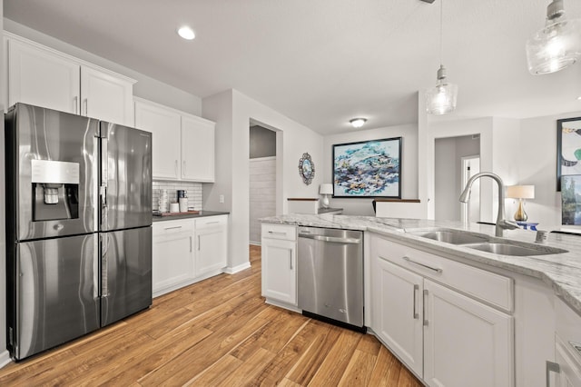 kitchen featuring a sink, decorative backsplash, appliances with stainless steel finishes, white cabinetry, and light wood-type flooring