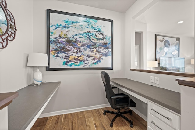 home office with wood finished floors, built in desk, and baseboards