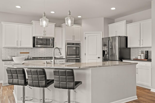 kitchen featuring a breakfast bar, light wood-style flooring, appliances with stainless steel finishes, white cabinets, and a kitchen island with sink