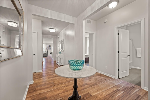 hall featuring wood finished floors, visible vents, and baseboards