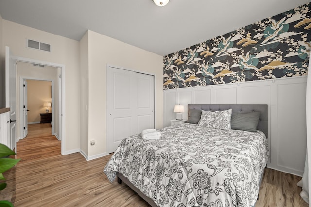 bedroom with visible vents, light wood finished floors, a closet, wainscoting, and a decorative wall