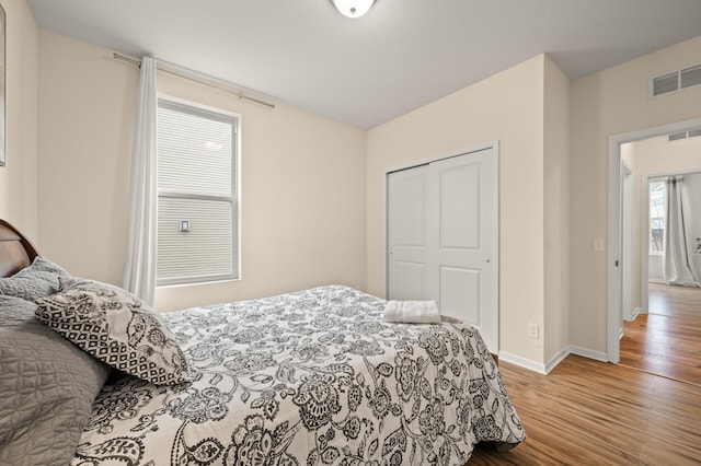 bedroom with wood finished floors, visible vents, a closet, and baseboards