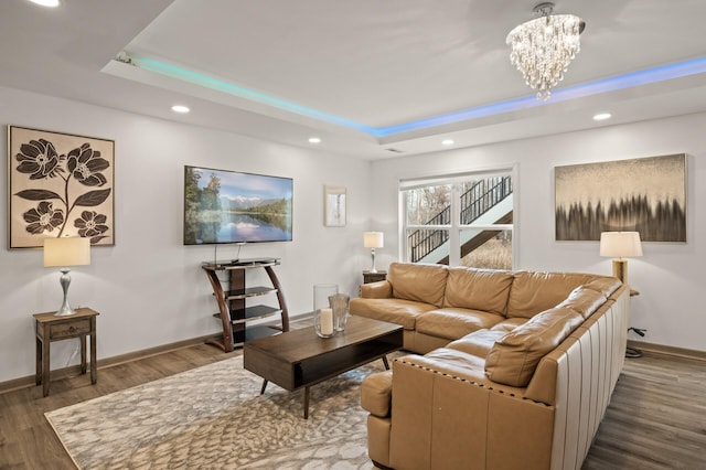 living area with a tray ceiling, wood finished floors, recessed lighting, baseboards, and a chandelier